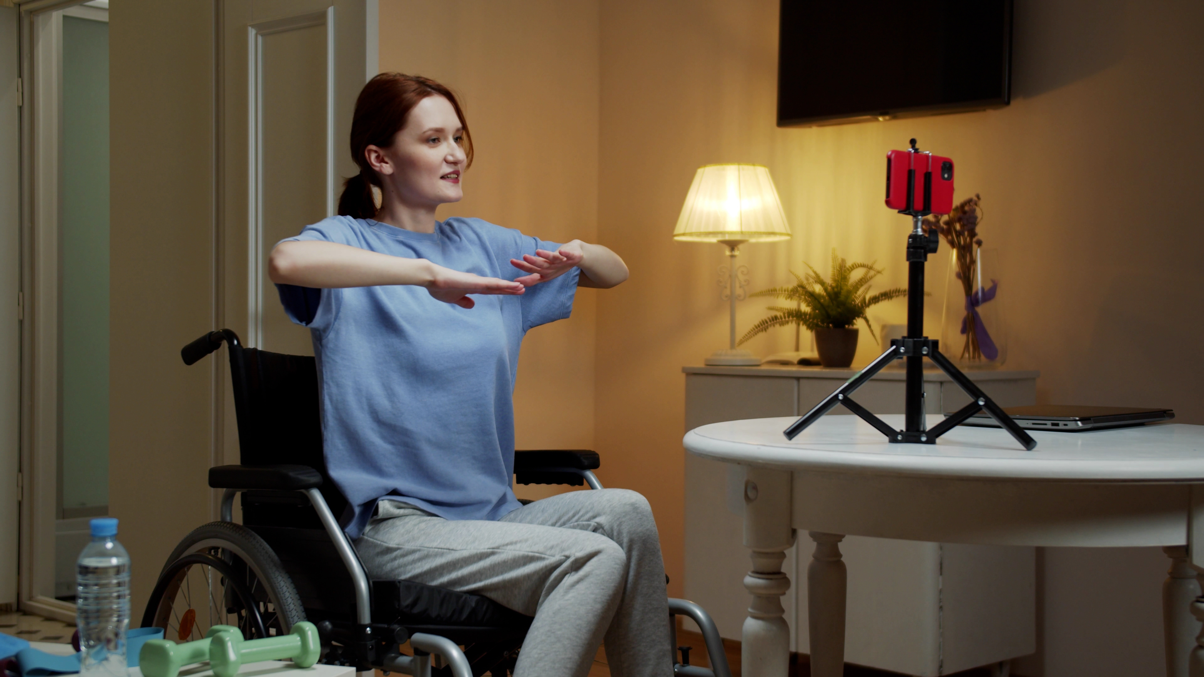 female wheel chair user watching phone on a tripod and holding up her arms to exercise